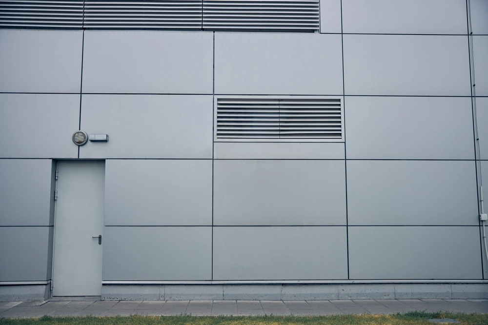 Nowoczesna elewacja z szarych paneli metalowych z drzwiami i kratką wentylacyjną – ocieplenie ścian